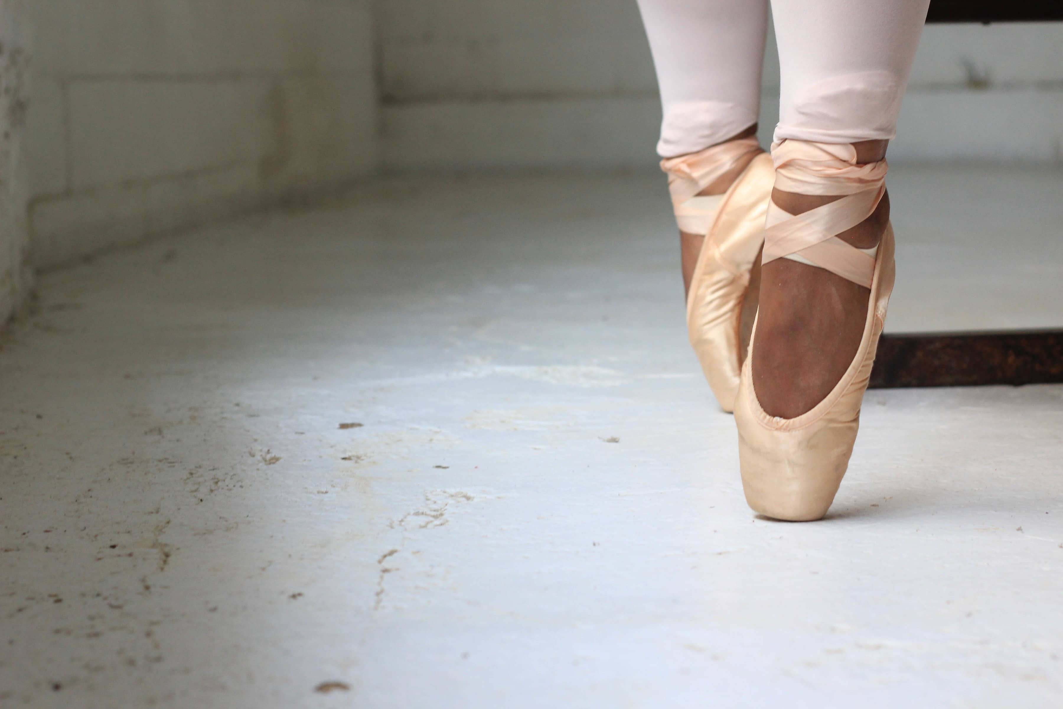 Füße einer Ballerina in Ballettschuhen. Sie steht auf den Zehen.