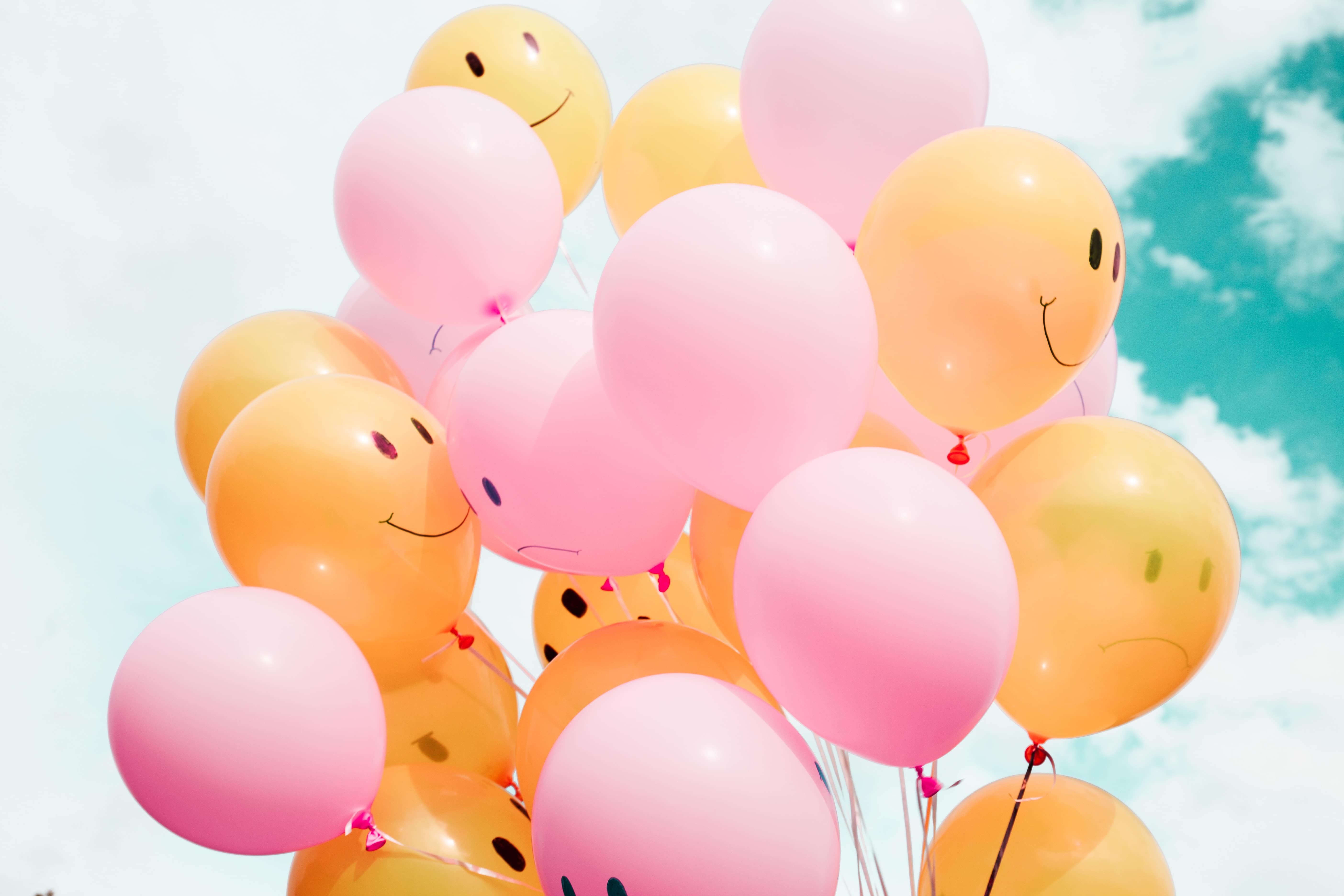 Rosa und orangene Luftballons im Himmel mit aufgemalten lachenden und weinenden Gesichtern