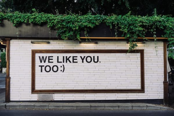 Auf einer Hauswand steht in Großbuchstaben "WE LIKE YOU, TOO :)"