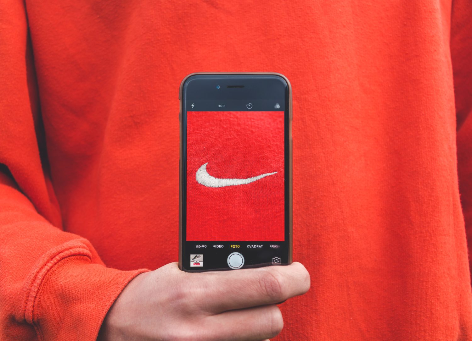 Brand Nike auf roten Pullover wird von Smartphone fotografiert