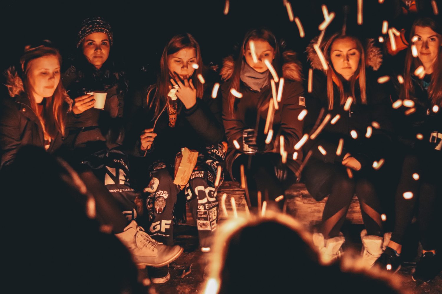 Junge Frauen sitzen um ein Lagerfeuer herum.