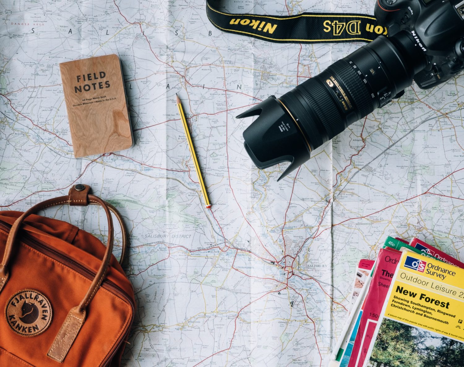 Reiseführer, Rucksack und Stifte liegen auf einer Landkarte.