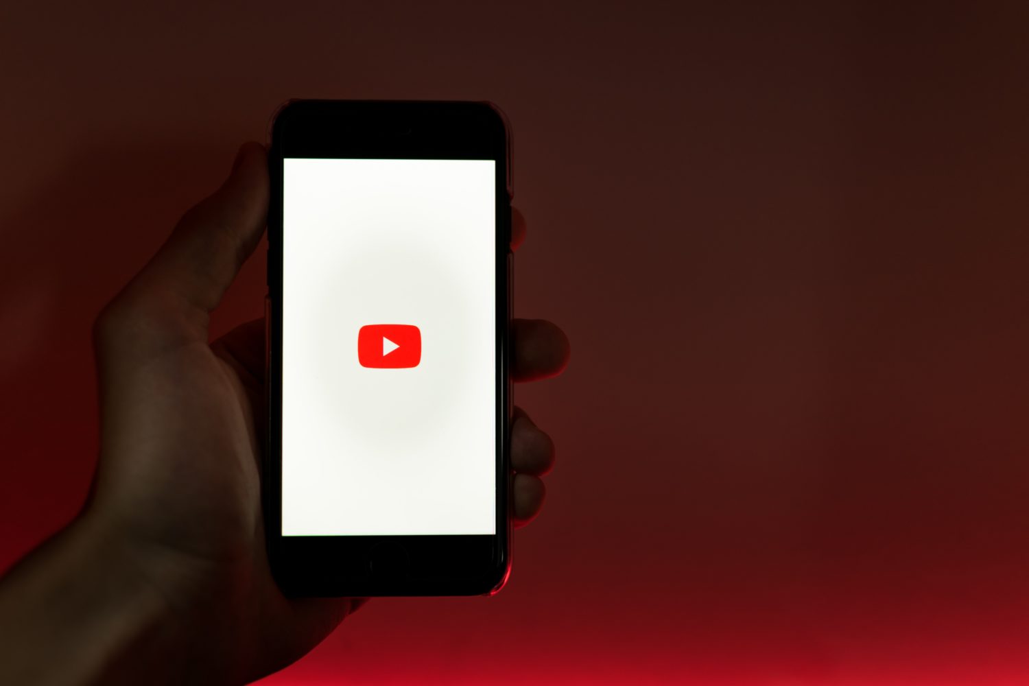 Hand hält ein Smartphone mit dem Youtube-Symbol auf dem Display.