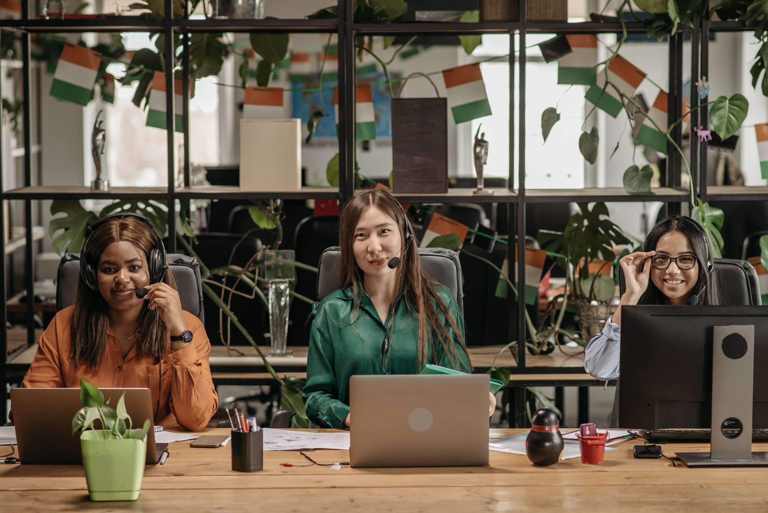 Frauen sitzen an Laptops mit Headset und lachen ; Kundenservice in einem Unternehmen über alle Kanäle 