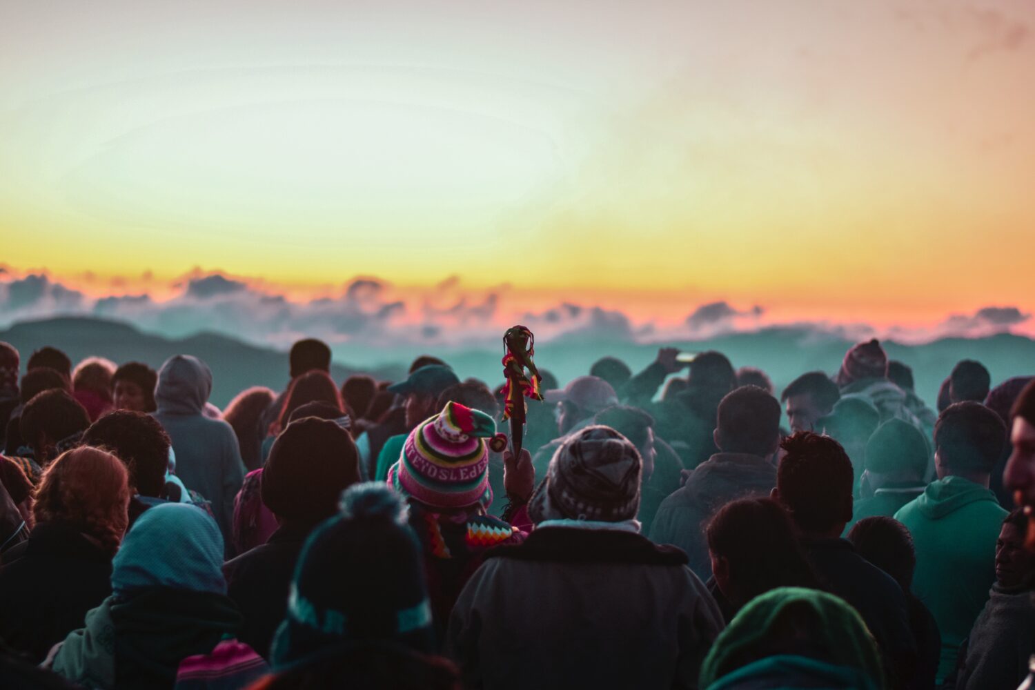 Menschen schauen einen Sonnenuntergang an, viele tragen bolivianische Mützen, einer hält ein Zepter