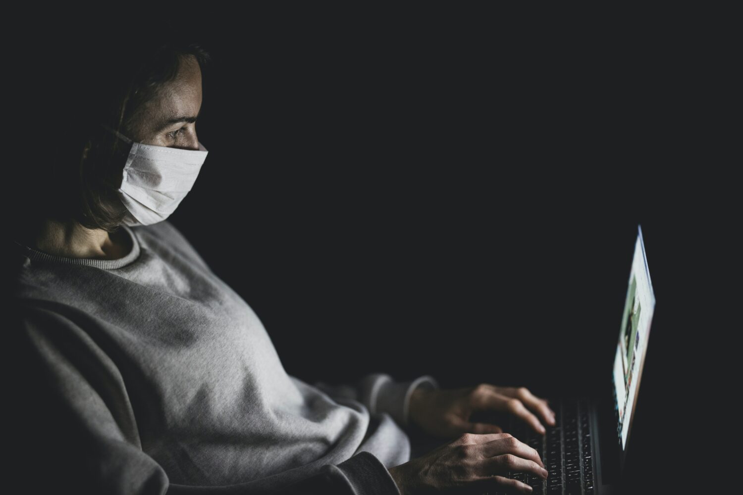 Frau sitzt mit Maske vorm Laptop 