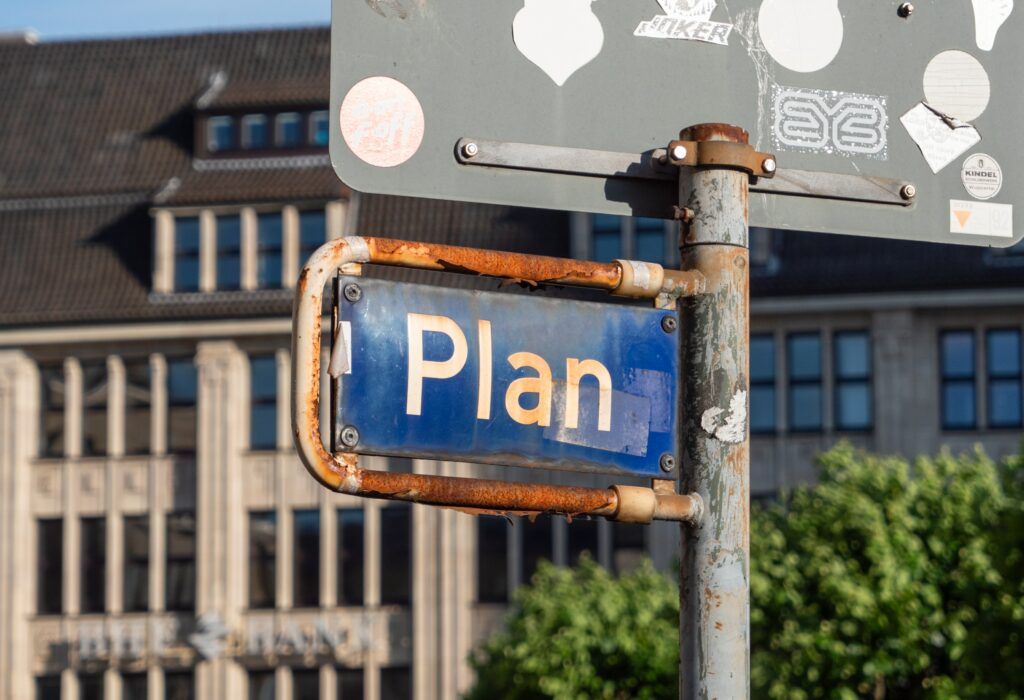 Vor einem Gebäude steht ein blaues Straßenschild. Darauf steht das Wort "Plan".